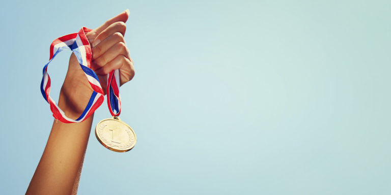 A person's hand stretching into the air holding a gold medal