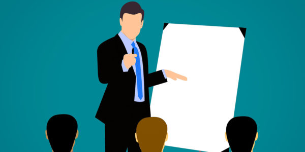 A person standing in front of a group of people presenting with a white board.