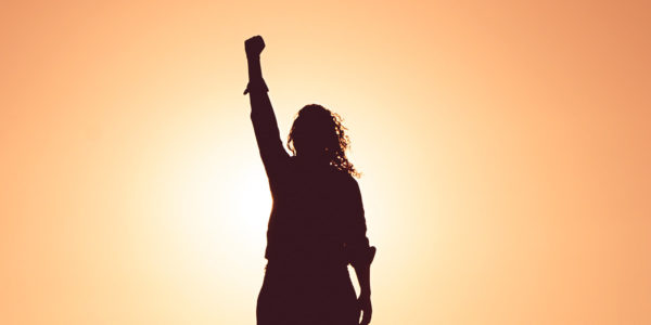 The silhouette of a woman standing with her fist in the air at sunset