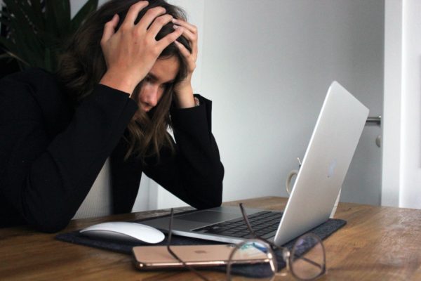 A woman in a black long sleeve sits in front of her laptop with her head in her hands