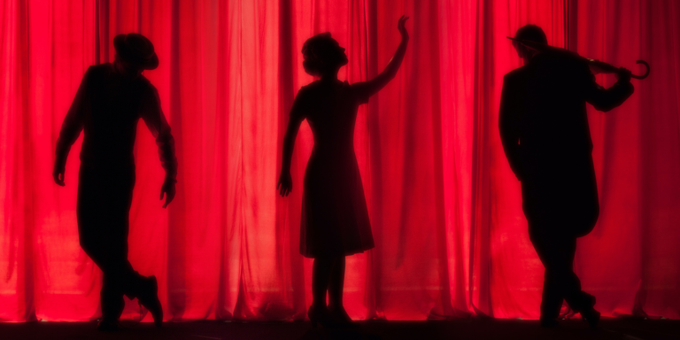 The silhouette of a  woman sings while two men on either side of her act out their roles with a red theater backdrop.