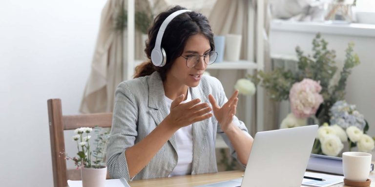 A women sits in front of a laptop with headphones on as she talks