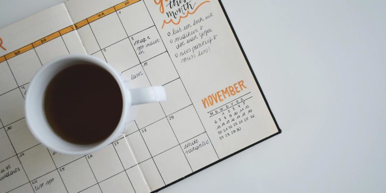 A cup of coffee sits on top of a calendar planner that is open to the month of November