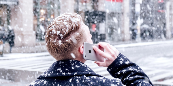 A man has his back turned as he is on the phone in a snow storm