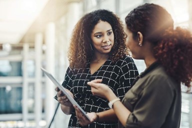 Two women hold a document and discuss what to do next.