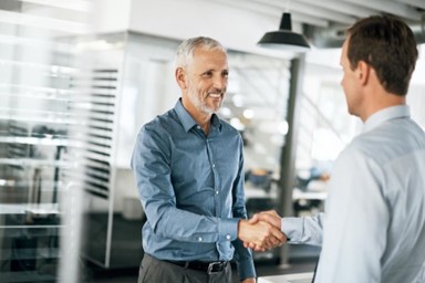 A man smiles and shakes another man’s hand.