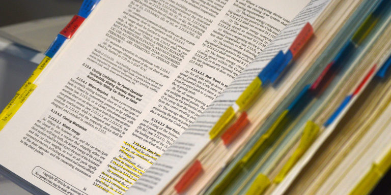 A book lay open with color coded with sticky notes on multiple pages.