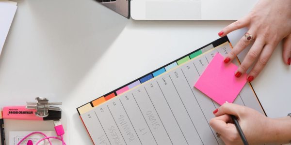 A hand writes on a sticky note over top of  a blank calendar.