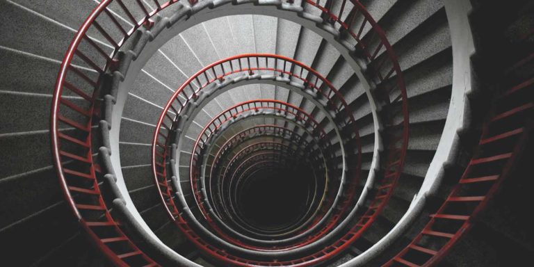 A gray staircase with a red hand railing spirals downward.