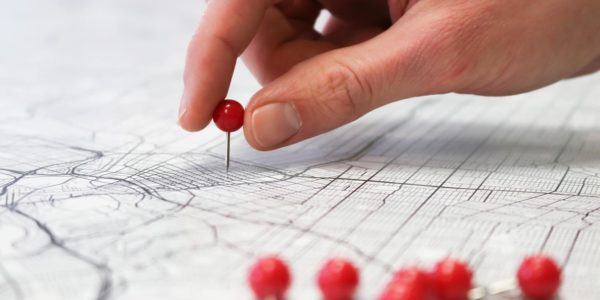A hand places a red push pin on a map with many other red push pins near it.