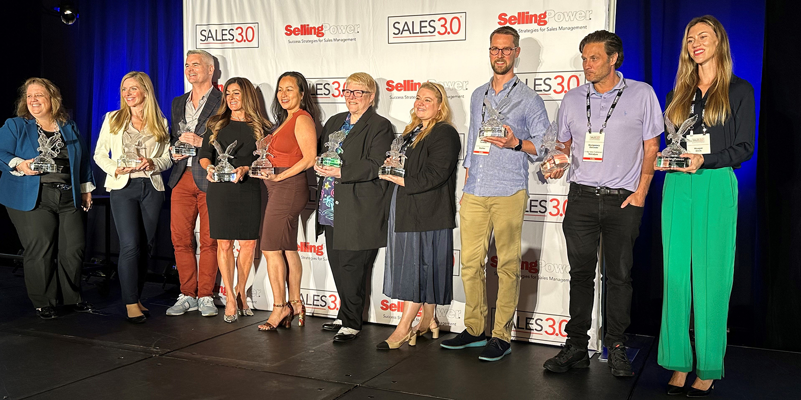 Ten people stand in a line on stage holding awards. 