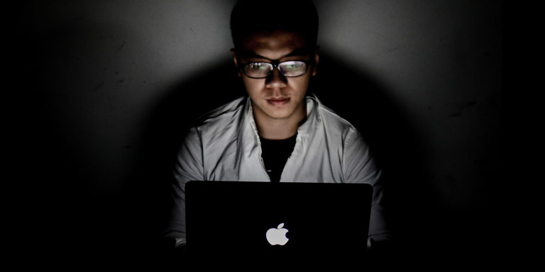 A person sits behind a laptop with the lights off.