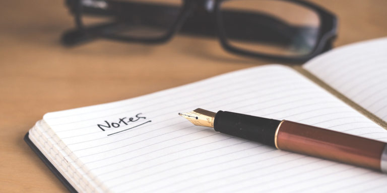 A pen lays on an open notepad with the word 