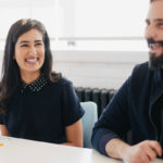 Two people sit at a table smiling.