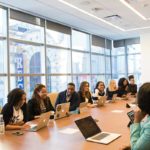 At a conference table sits a large group of men and women.