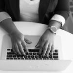 A black and white image of hands on a laptop keyboard.