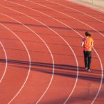 Woman in orange shirt and black pants running on track.