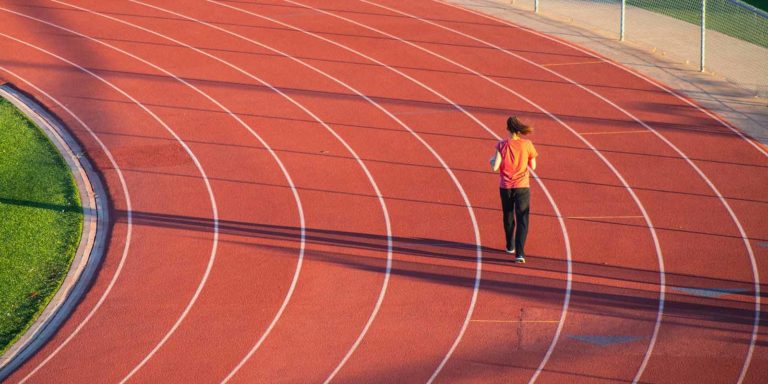 Woman in orange shirt and black pants running on track.