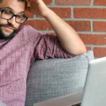 A frustrated man looks at his laptop while on the phone.