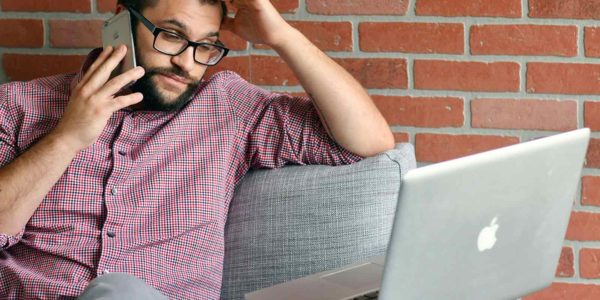 A frustrated man looks at his laptop while on the phone.