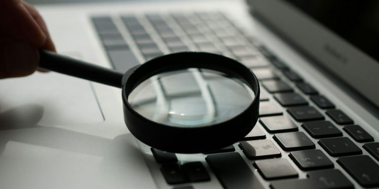 A black magnifying glass is held over a laptop keyboard.