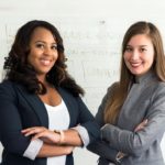 Two women stand next to each other with arms folded smiling.