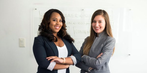 Two women stand next to each other with arms folded smiling.