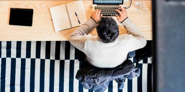 An aerial shot of a man hunched over his laptop at a table.