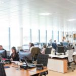 An office space with desks and chairs and people.