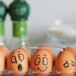 Five brown eggs sit in a carton each with different facial expressions drawn on them.