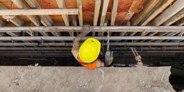 A person in a yellow hard hat drills into a pipe.