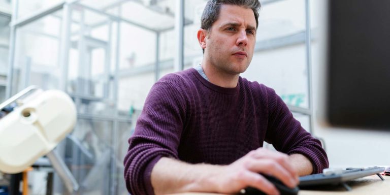 A man focuses on the computer screen while holding a computer