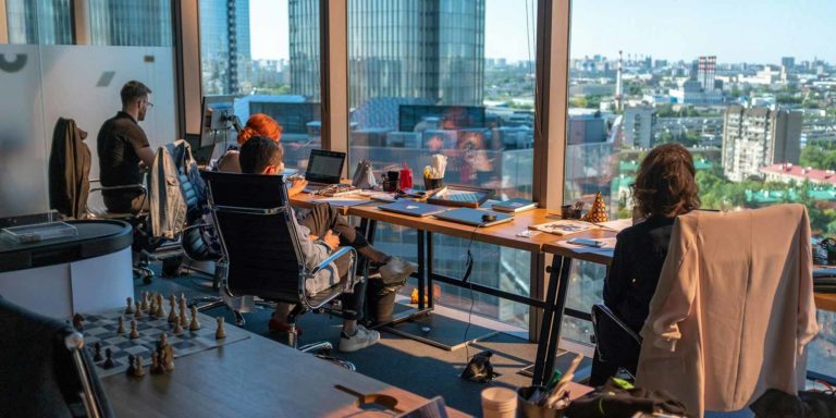 Four people sit at a long table facing the windows as they work.