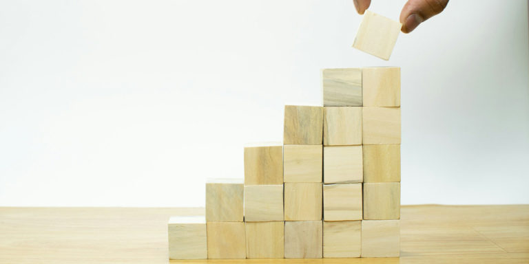 Hands stack wooden blocks into an increasing tower.