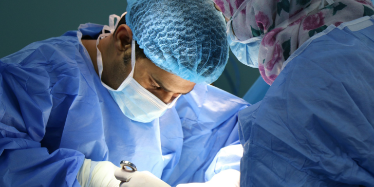 A Surgeon works while wearing scrubs and a scrub hat.