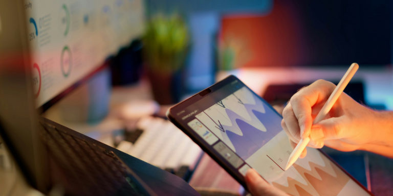 A person sketches on a tablet in front of a computer screen.