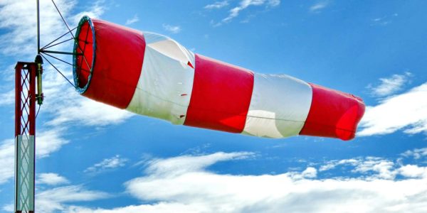 A red and white flag flying under a blue sky with clouds.